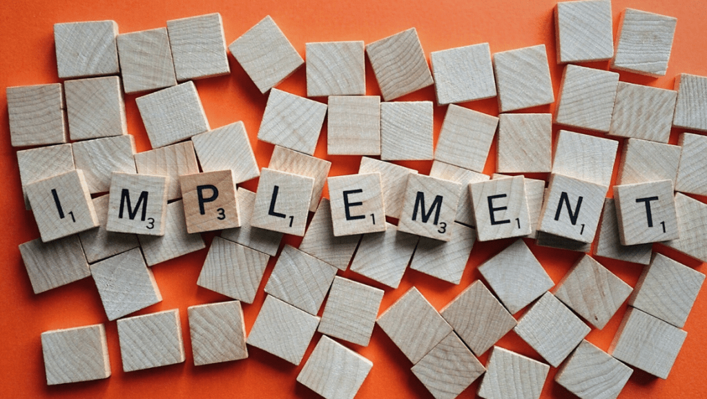 The word "implement" spelled out in scrabble tiles